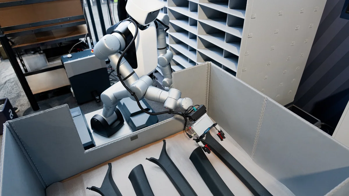 High angle perspective of Agile humanoid picking semi-rigid vehicle trim parts from industrial containers at Audi